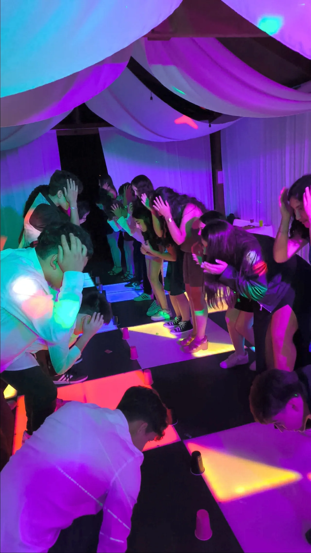 Jóvenes participando en una dinámica grupal sobre una pista iluminada durante una graduación.