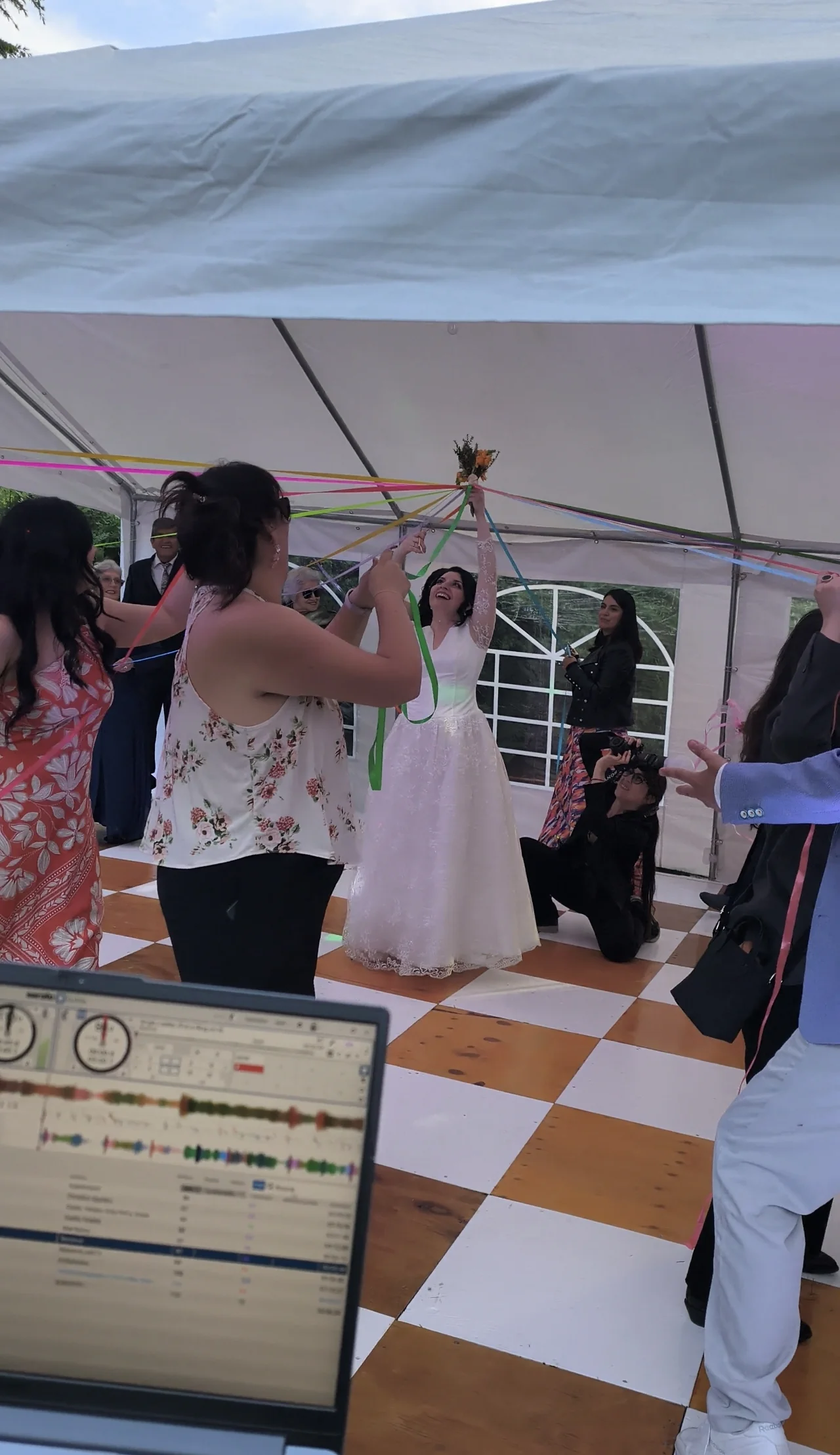 Novia con un ramo e invitados con cintas de colores durante un matrimonio en una carpa