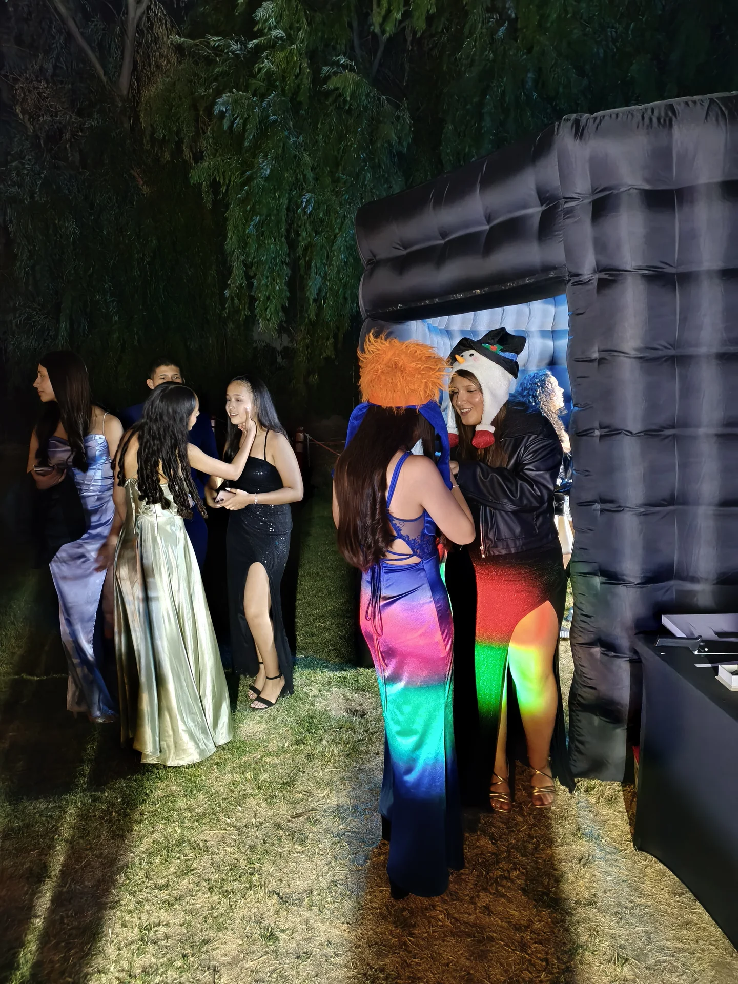 Invitadas con cotillón junto a la cabina inflable instalada en un jardín de noche