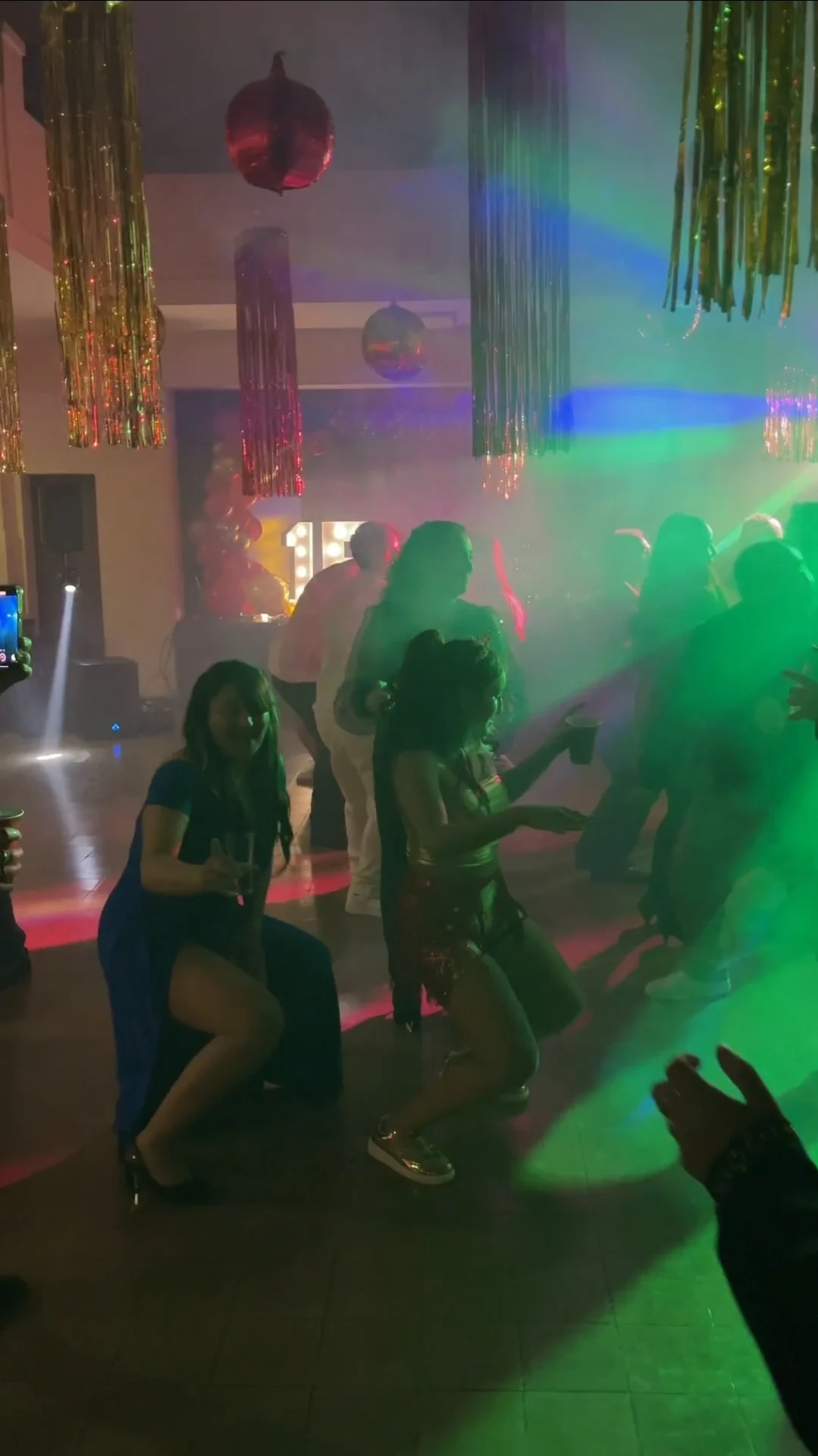 Invitados bailando bajo luces verdes y violetas en un salón decorado con el número 15